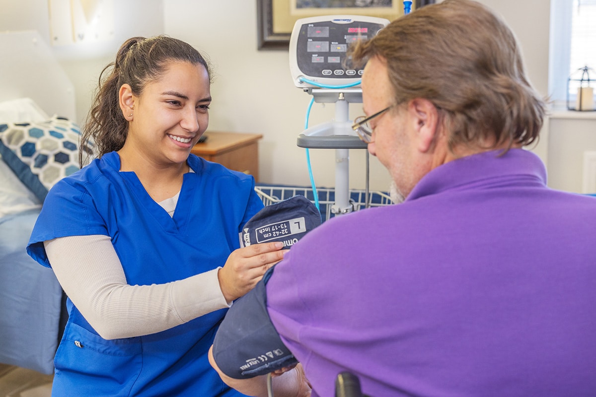 a caregiver taking the blood pressure of an elderly man at West Village Care